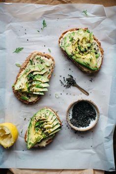 an open face sandwich with avocado and other toppings on it next to a lemon wedge