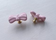 two pink bowknots are sitting on a white surface, one is gold