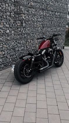 a red and black motorcycle parked in front of a wall with silver squares on it