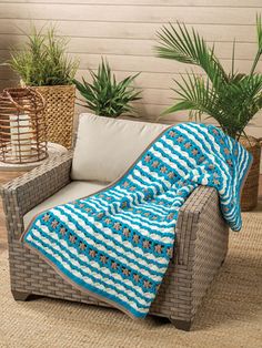 a blue and white blanket sitting on top of a chair next to a potted plant