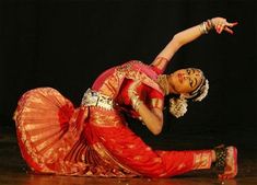 a woman in an orange and red dress is doing a dance pose on the floor