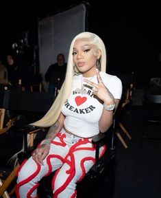 a woman with long blonde hair sitting in a chair and pointing at the camera while wearing red and white patterned leggings