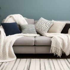 a couch with many pillows on it in front of a blue wall and white rug