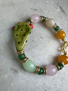 Bracelet with prickly pear in hand-painted ceramic with pure gold luster, mounted in gilded brass with various types of stones such as Agates and quartz Handmade Gold Jade Crystal Bracelet, Hand Painted Green Bracelet As Gift, Unique Agate Gemstone Bracelets, Artisan Multicolor Agate Bracelets, Unique Multicolor Agate Bracelets, Unique Enamel Bracelets As Gift, Unique Agate Bracelet For Gift, Elegant Handmade Enamel Bracelets, Handmade Enamel Bracelet As Gift