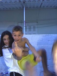 two young boys are playing with each other in front of a white brick wall and ceiling