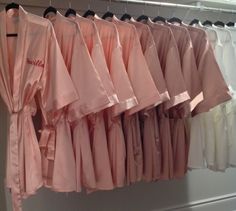 pink robes hang on a rack in front of white shirts and black pants hanging from hooks