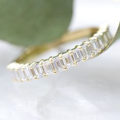 a gold ring with baguettes on it sitting next to a green plant leaf