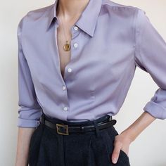 a woman in a purple shirt and black pants with her hands on her hips, looking at the camera