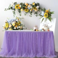 the table is covered with purple tulle and decorated with sunflowers, roses, and greenery