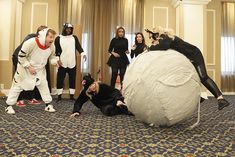 group of people dressed in costumes standing around a giant ball of yarn on the floor