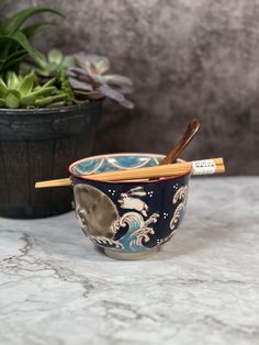 two bowls with chopsticks in them sitting on a table next to a potted plant