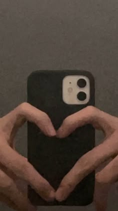 two hands making a heart shape with their fingers on a cell phone case in front of a gray wall