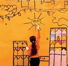 a woman drawing on the side of a yellow building with her hands in the air