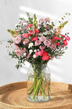 a glass vase filled with pink and white flowers on top of a wicker table