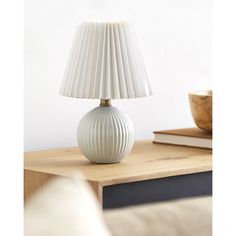 a white lamp sitting on top of a wooden table next to a book and bowl