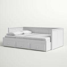 a white bed with drawers underneath it on a plain surface in front of a wall