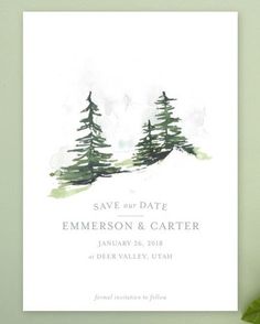 save the date card with watercolor pine trees on white paper and green leaves next to it