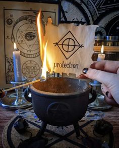 a person holding a lit candle in front of an iron pot with the word protection on it