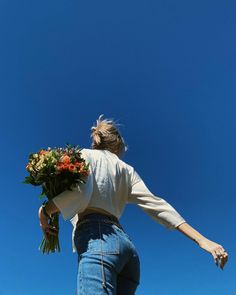 a woman is holding flowers in her hands and reaching up into the air to catch it