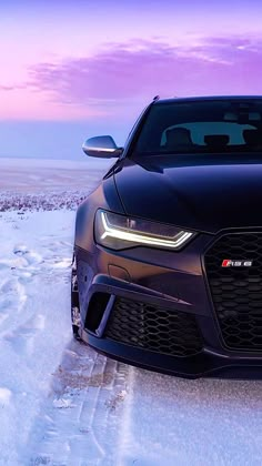 the front end of a black sports car on snow covered ground with purple sky in background