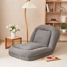 a living room with a gray chair and a white tray on the floor next to a lamp