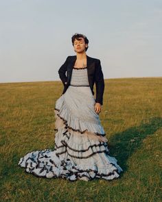 a woman in a dress standing on top of a grass covered field