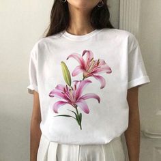 a woman standing in front of a white wall wearing a t - shirt with pink flowers on it