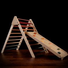 a wooden toy slide and ladder sitting on top of a wood floor in front of a black background