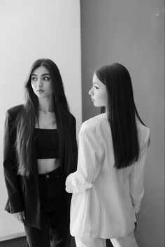 two women standing next to each other in front of a wall and one is wearing a jacket