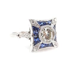 This stunning Art Deco style ring is the perfect ambassador of the period's elegant rectilinear design elements. Centered with an 0.85ct Old European cut diamond, the bezel set center stone is surrounded by a flourish of French cut sapphires and diamonds. The undercarriage is beautifully filigreed and the narrow shoulders of the ring widen to a 2mm wide double half round shank.CENTER STONE: 0.85 ct Old European cut diamond - J color, VS2 clarityMETAL: 18K White GoldSIDE STONES: Diamonds (F-G col Luxury Sapphire Diamond Ring With Diamond Cut, Diamond Cut Sapphire Ring With Cushion Shape, Art Deco Diamond Jewelry With Gemstone, Luxury Gia Certified Diamond White Sapphire Ring, Gia Certified Art Deco Platinum Jewelry, Luxury Asscher-cut Sapphire Ring With Diamond Details, Classic Gia Certified Rectangular Sapphire Ring, Platinum Diamond White Diamond Ring, Platinum Diamond Ring In Diamond White