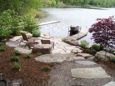 there are two chairs on the rocks by the water