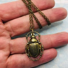 "Brass beetle or scarab locket necklace. Perfect for the entomologist or bug lover! Beautiful brass beetle with nice detail. Paired with a tear drop shaped locket. Fantastic detail on this insect! The ancient Egyptians used the image of the beetle, or scarab as a protection or amulet. It symbolizes immortality and transformation. The brass charm measures 1 1/4' by 3/4\". The locket inside measures a tiny 1/2\" by 1/4\". I offer two types of chains for this necklace. You may choose a plain brass Scarab Beetle Jewelry, Beetle Accessories, Beetle Scarab, Scarab Necklace, Bug Necklace, Beetle Necklace, Rhino Beetle, Bug Jewelry, Handwritten Gifts