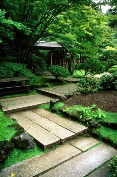 a stone path in the middle of a lush green park with steps leading up to a gazebo