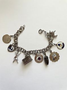 Long before the days of Pandora bracelets, women wore charm bracelets. These bracelets were often used to commemorate specific events in one's life, places one traveled, or other things that reflected your personality. This particular charm bracelet has 9 charms. Most of the charms are from travel . It also has other items that depict the personality of the previous owner. The bracelet measures 7 1/2 inches long and is 1 1/8 inches long at the longest charm. The bracelet weighs 35.3 grams  Every charm and the bracelet is either marked sterling or 925. This item is in excellent preowned vintage condition with normal wear for the age Charm Bracelet Men, Vintage Jewelry With Dangling Charms As Souvenir, Vintage Jewelry With Dangling Charms Souvenir, Vintage Dangling Charms Jewelry Souvenir, Heirloom Style Charm Bracelet With Vintage Charm As Gift, Heirloom Style Vintage Charm Bracelet For Gift, Heirloom Style Vintage Charm Bracelet As Gift, Vintage Metal Charms With Removable Details, Vintage Jewelry Bracelet With Dangling Charms