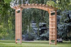 a wooden arbor in the middle of a grassy area with trees and bushes behind it