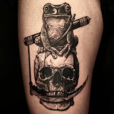 a frog sitting on top of a skull with a knife in it's mouth