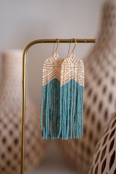 two pairs of earrings with tassels are hanging from a gold stand next to vases