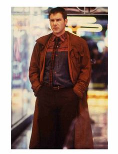 a man standing in front of a store window wearing a red coat and plaid shirt