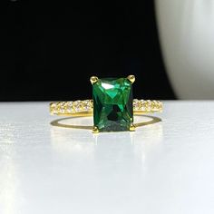 an emerald colored ring with diamonds on the sides and gold band, sitting on a white surface