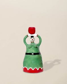 a green ceramic figurine with a red hat on it's head and arms in the air