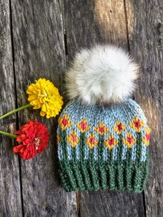 a knitted hat with a pom - pom on top and flowers next to it