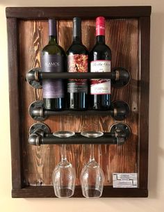 two wine glasses and three bottles on a wooden shelf with metal fittings, hanging from the wall