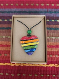 "This listing is for a single rainbow colored ceramic heart pendant necklace. Each pendant is hand carved and unique. You will receive one very similar to the one featured in the photo with stripes of red, orange, yellow, green, blue, and purple.  The pendant is made of a white highfire stoneware clay. The pendant is carved and glazed on both the front and back.   It is strung onto a 20\" waxed black cotton cord with a silver toned lobster claw clasp and chain.  This listing is perfect for Valentines Day class gifts, multi child families, bridesmaid gifts and more. It will also make a beautiful and meaningful gift as a token of love and acceptance for members of the LGBTQ community. Representation matters. Please reach out to me if you are interested in a custom made heart order." Rainbow Heart Beads Jewelry Gift, Rainbow Heart Beads Jewelry For Gift, Gift Rainbow Jewelry With Heart Beads, Adjustable Multicolor Heart Pendant Necklace, Adjustable Multicolor Heart Necklace, Multicolor Heart Pendant Jewelry For Gift, Adjustable Heart-shaped Multicolor Necklace, Colorful Pendant Jewelry As A Gift, Handmade Multicolor Heart Pendant Necklace