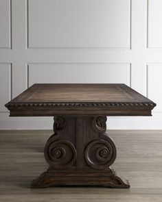 an old wooden table with carvings on the top and bottom, in front of a white wall