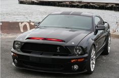 a black mustang parked in front of a body of water