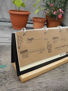 a menu board with clippings attached to it sitting on a table next to potted plants