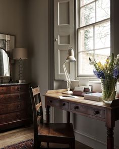 a room with a desk, chair and mirror in it next to a large window