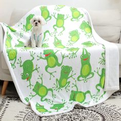 a white dog sitting on top of a couch under a green frog blanket