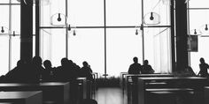 black and white photo of people sitting at desks in front of large glass windows