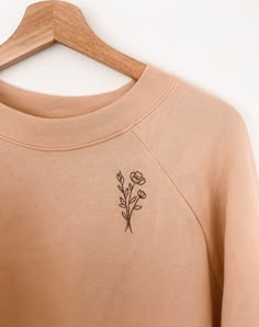 a t - shirt hanging on a wooden hanger with a flower embroidered on it